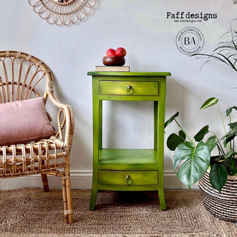 Pistachio Terra Clay Paint provides endless possibilities for your imagination and can be used on wood, canvas, tile, fabric and more! Light green clay painted end table blended with yellow clay paint. Staged with a bowl of apples and a plant also has a wicker chair next to it.