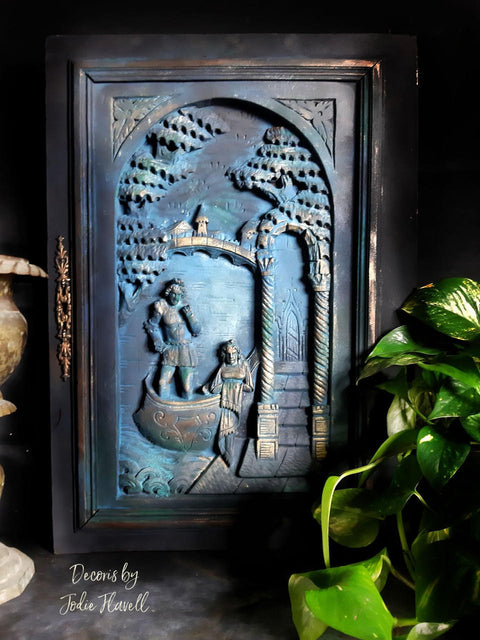 Prairie Dawn Terra Clay Paint provides endless possibilities for your imagination and can be used on wood, canvas, tile, fabric and more! Black, blue and cream clay painted plaque with a picture of a man and woman in a boat with a village in the back.