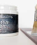 Terra Clay Paint Terra Seal - Jar of Terra Seal clay paint sealer sitting on table without lid sitting next to a paint brush applying Terra Seal to a piece of wood.