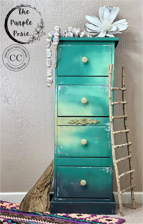 Wheat Terra Clay Paint provides endless possibilities for your imagination and can be used on wood, canvas, tile, fabric and more!  A blue, wheat and black blended chalk painted dresser with wheat drawer knobs.  Sitting on a tan carpeted floor with a purple and tan rug.  A wooden ladder is leaned up against the right side of the dresser, and a piece of wood is against the left side.  A white flower and white beads are on top of the dresser.