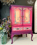 Purple, pink, and yellow painted armoire. The Gilded Age Transfer has been applied to the doors and drawers