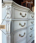 Close-up of a vintage-style dresser with ornate details, painted in a light gray color. The dresser features decorative, curved handles. A label points to the corner, highlighting "Gray Best Dang Wax."