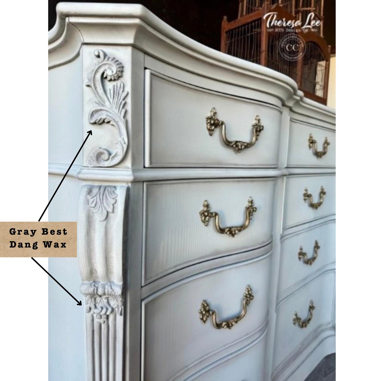 Close-up of a vintage-style dresser with ornate details, painted in a light gray color. The dresser features decorative, curved handles. A label points to the corner, highlighting "Gray Best Dang Wax."