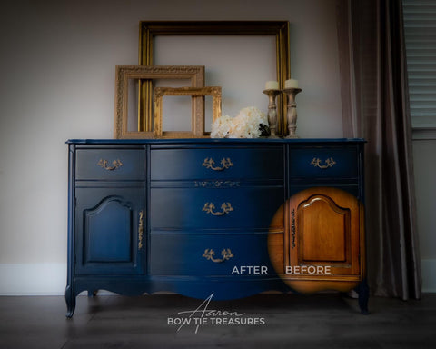 a moody dark blue chalk painted dresser.  blended with a lighter blue.  the bottom right corner of the dresser is a spotlight of the wood beneath the painted furniture.  On the top of the dresser is three empty picture frames, some flowers and two candle sticks.