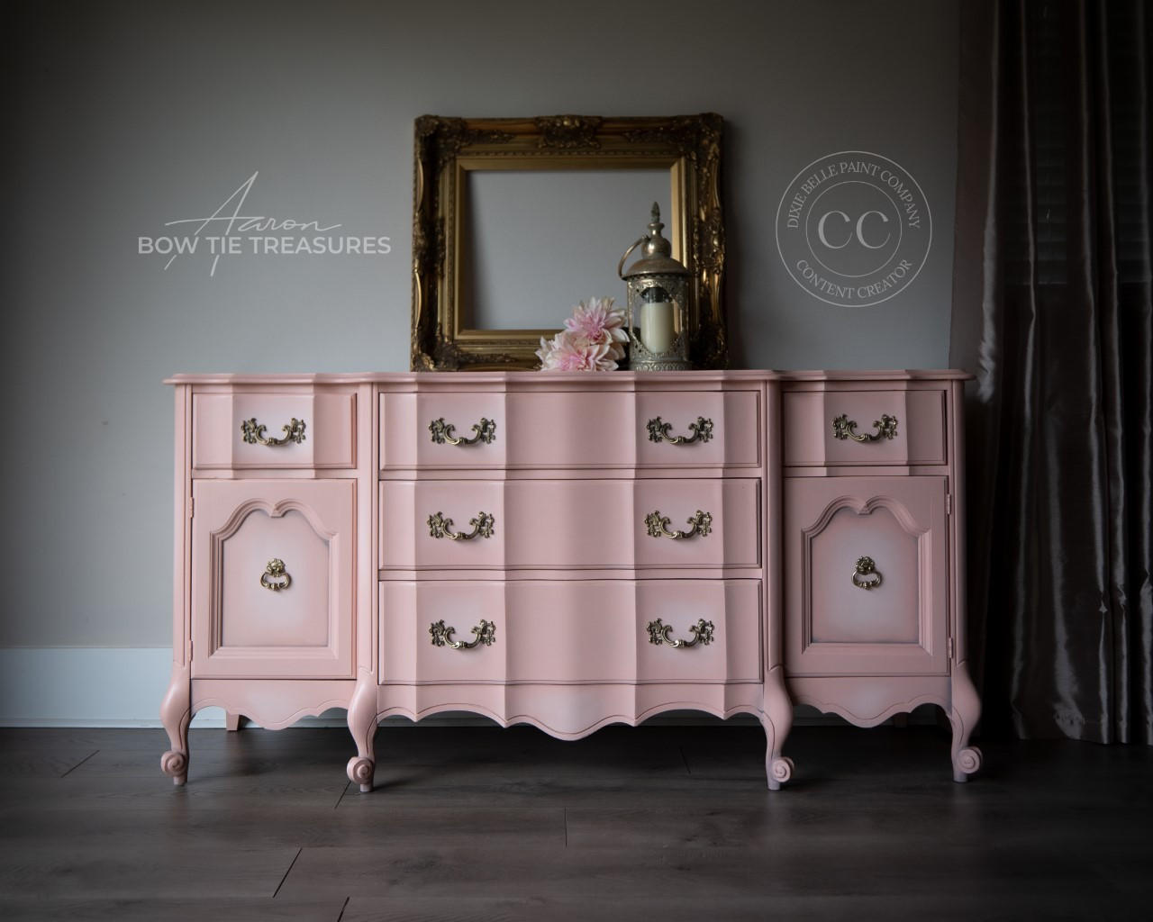 A pink dresser that is blended with some white chalk paint in the middle near the handles creating a ombre effect.  staged with an empty gold picture frame and candle light and some flowers.