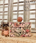 Belles and Whistles Tropical on Pink - Rice Decoupage Paper.  Small chest of drawers with the tropical On Pink Rice Decoupage Paper on front, staged with two planters on the left, one with cactus and one with dried floral arrangement