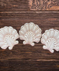 Three decorative, wooden shell-shaped appliques are arranged in a row on a rustic wooden surface with visible grain patterns.