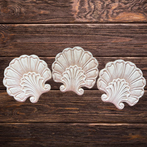Three decorative, wooden shell-shaped appliques are arranged in a row on a rustic wooden surface with visible grain patterns.