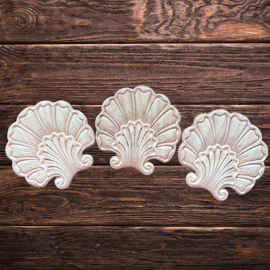 Three decorative, wooden shell-shaped appliques are arranged in a row on a rustic wooden surface with visible grain patterns.