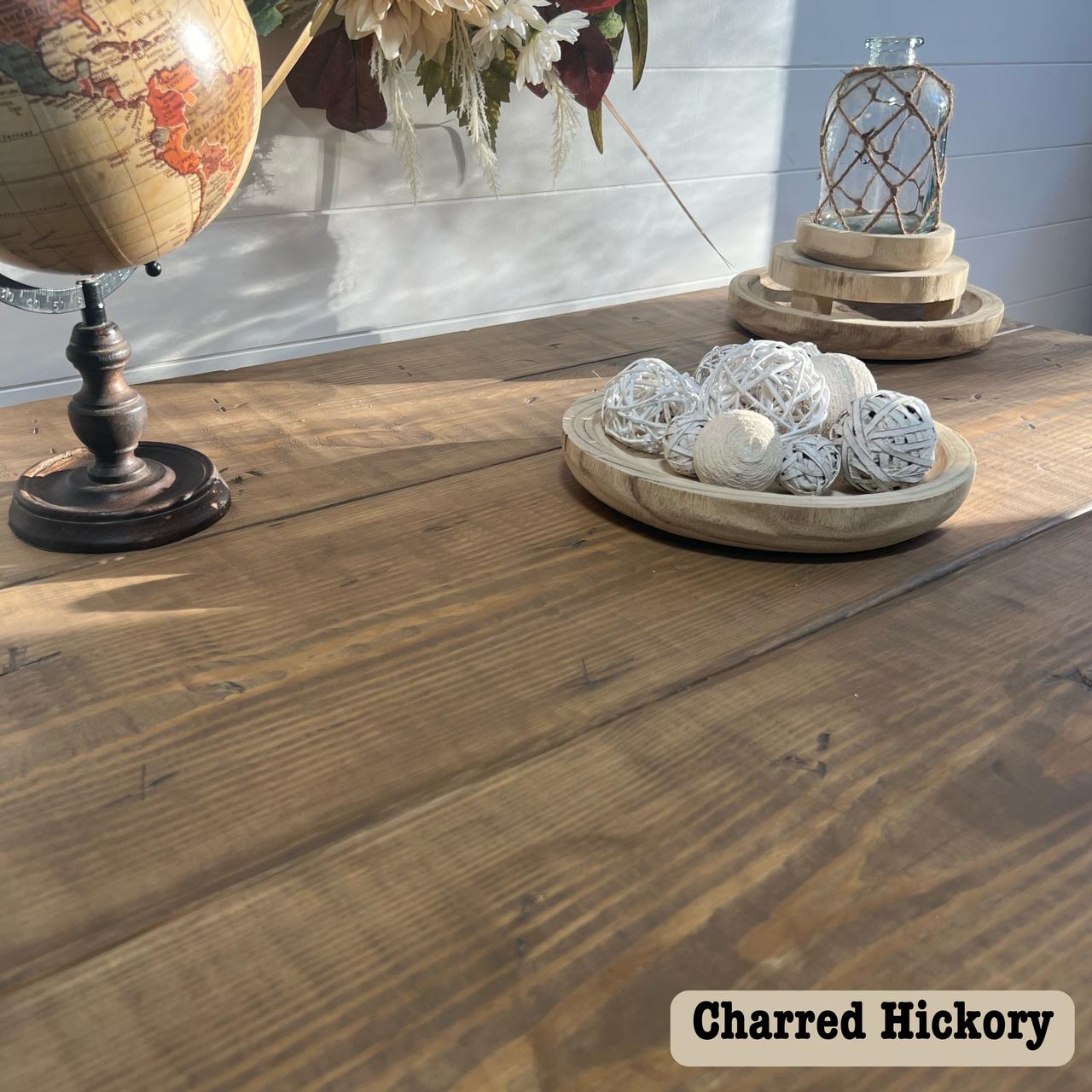 A wooden table displays a globe on a stand, a vase with flowers, and a wooden tray of decorative white balls. Sunlight dances across the surface, revealing the rich, water-based stain of Charred Hickory etched at the bottom right.