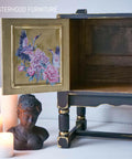 Black Distressed entertainment center with opened cabinet door. Inside of cabinet door is the Versailles Garden Transfer. Staged under the open cabinet door is 3 lit candles of different tiers with a bronze statue next to them.