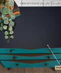 Overhead view of a dark blue, three-drawer chest labeled "Deep Sea," finished with Deep Sea Silk All-in-One paint. The teal drawers feature dark knobs. A potted plant and books rest atop. Text at the top reads "Gracie's House Painted Furniture.