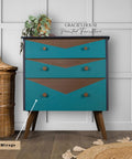 Mirage Silk All-In-One paint is perfect for painting kitchen cabinets, bathroom cabinets and painting furniture. A vintage-style dresser with teal and brown geometric patterns against a paneled wall, accented by a basket on the left and a plant on top. The text "GRACIE'S HOUSE Painted Furniture" and "Mirage Silk-All-in-One Mineral Paint" highlights elegance.