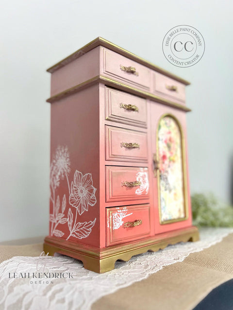 Pink painted jewelry box/chest with gold handles and accents. The Wildflowers Silkscreen Stencil has been applied in white on the front and side.