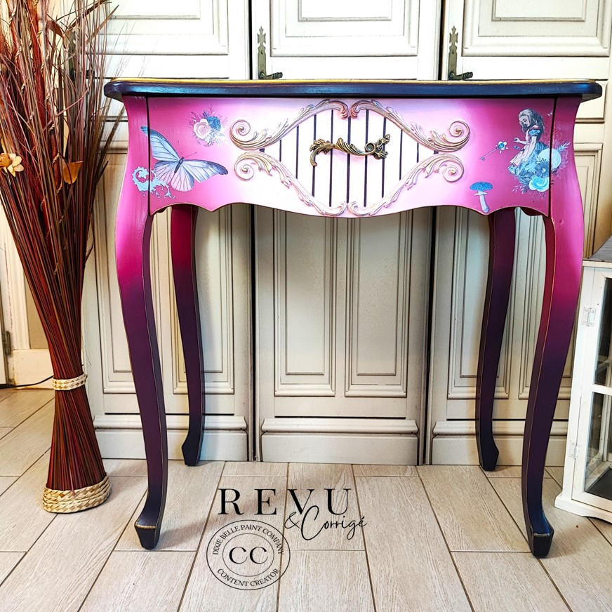 WoodUBend Applique #1723 (set of 2) is the perfect mouldable embellishment for any project!
An end table painted in a gradient effect with pink and purple along with the Alice 2 Transfer on the drawer. In the middle of the drawer 4 Applique #1723 seen around the hardware of the piece, they kind of look like lips with spirals are the end.