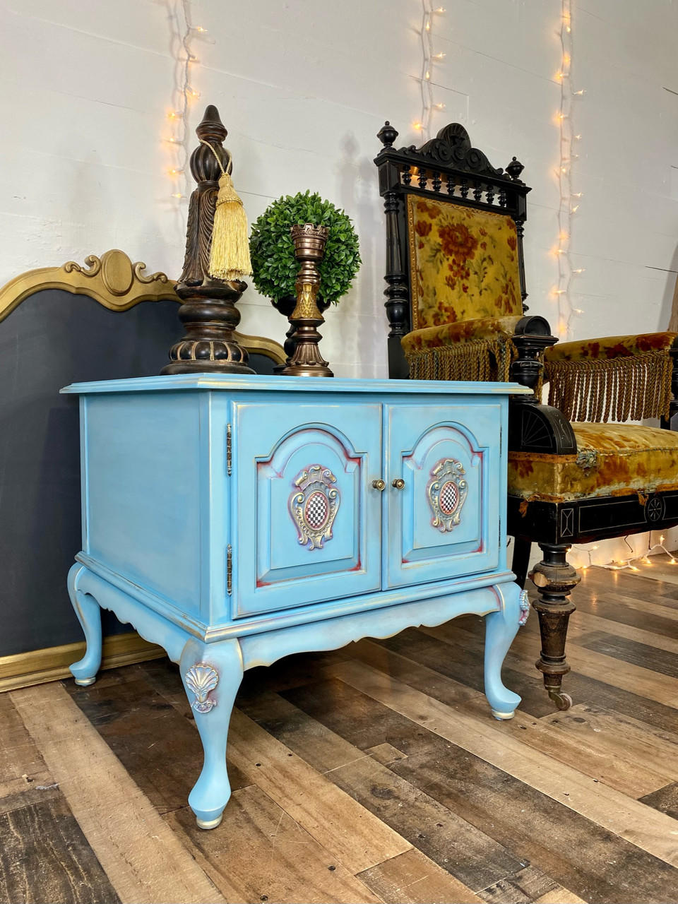 WoodUBend Applique #2447 (set of 2) is the perfect mouldable embellishment for any project!
A blue end table with Applique #2447 (set of 2) on the tops of both legs. Staged next to a yellow fabric chair, on top of the piece are bronze statues.