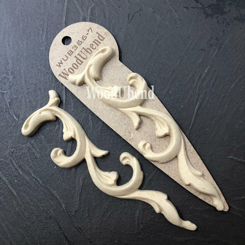 WoodUBend Applique #366-7 (set of 2) is the perfect mouldable embellishment for any project!
The  Applique #366-7 (set of 2) one in its packaging and the other without, staged on top of a black crinkled background.