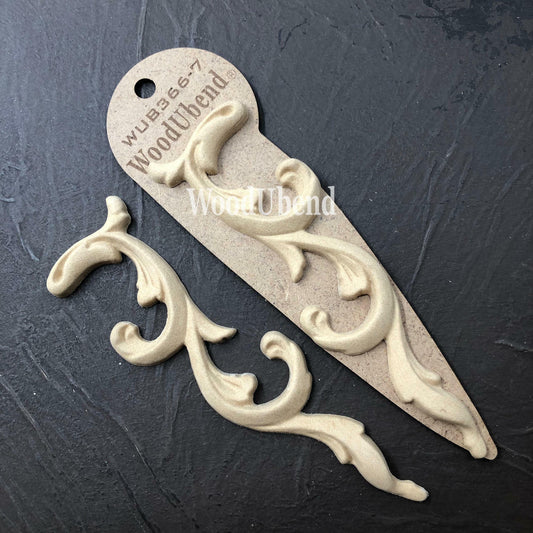 WoodUBend Applique #366-7 (set of 2) is the perfect mouldable embellishment for any project!
The  Applique #366-7 (set of 2) one in its packaging and the other without, staged on top of a black crinkled background.