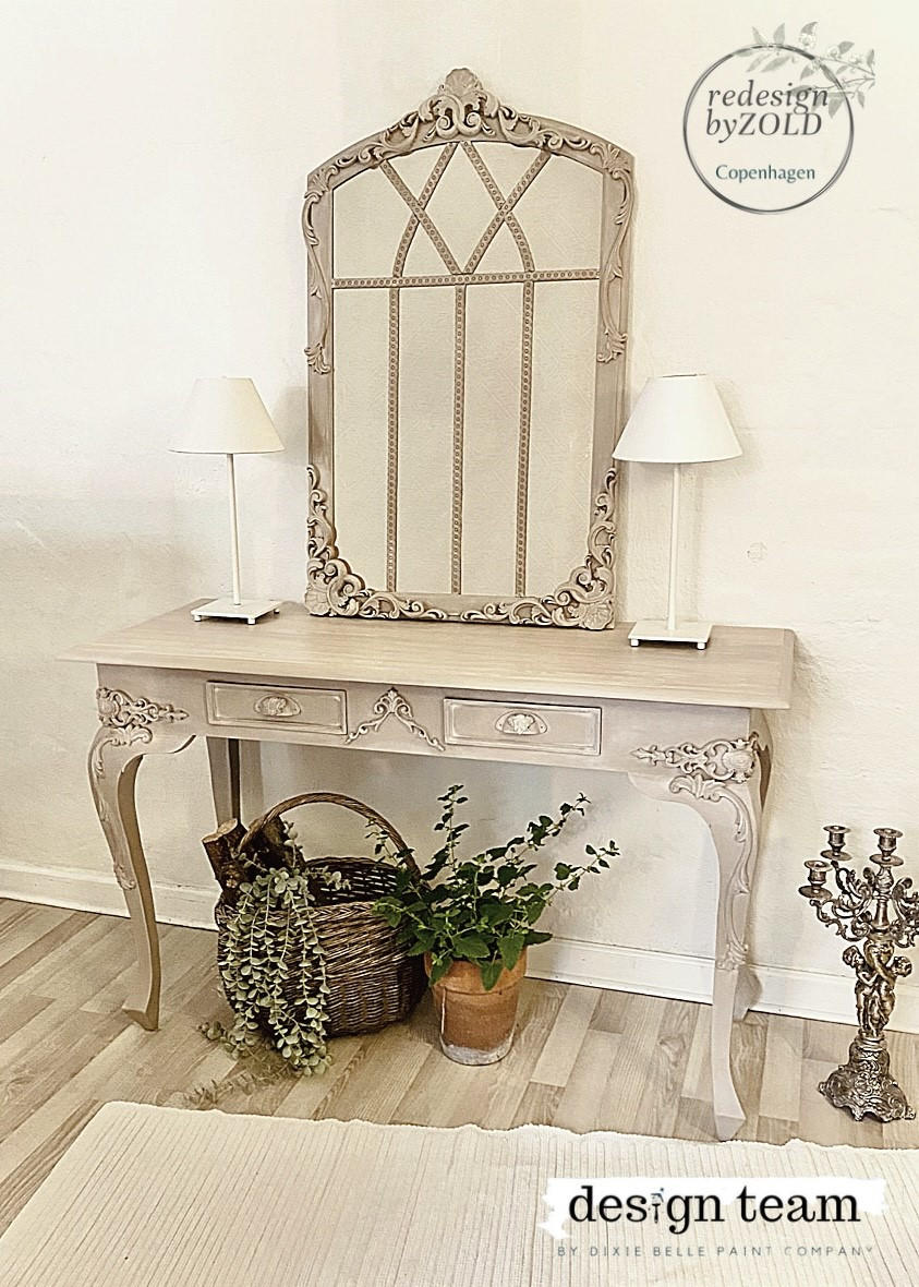 WoodUBend Applique #6069 (Set of 2) 
This applique is quite big.  This picture is of a table with a large mirror in the center.  The mirror is leaning up against the wall that the table is in front of. The table has two, white lamps which are on either side of the mirror.  There are 3 Appliques on the mirror; two on the bottom corners and one at the very top.  Everything is painted  with Moon Beam Terra Paint.  It is staged with plants and a candle opera.