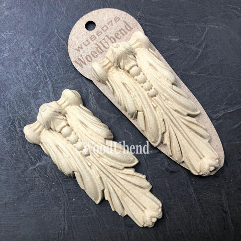 WoodUBend Applique #6076 (Set of 2) is the perfect mouldable embellishment for any project!
The Applique #6076 (Set of 2) staged on a black crinkled background. One of the appliques is seen out of the packing while the other is in the packaging.