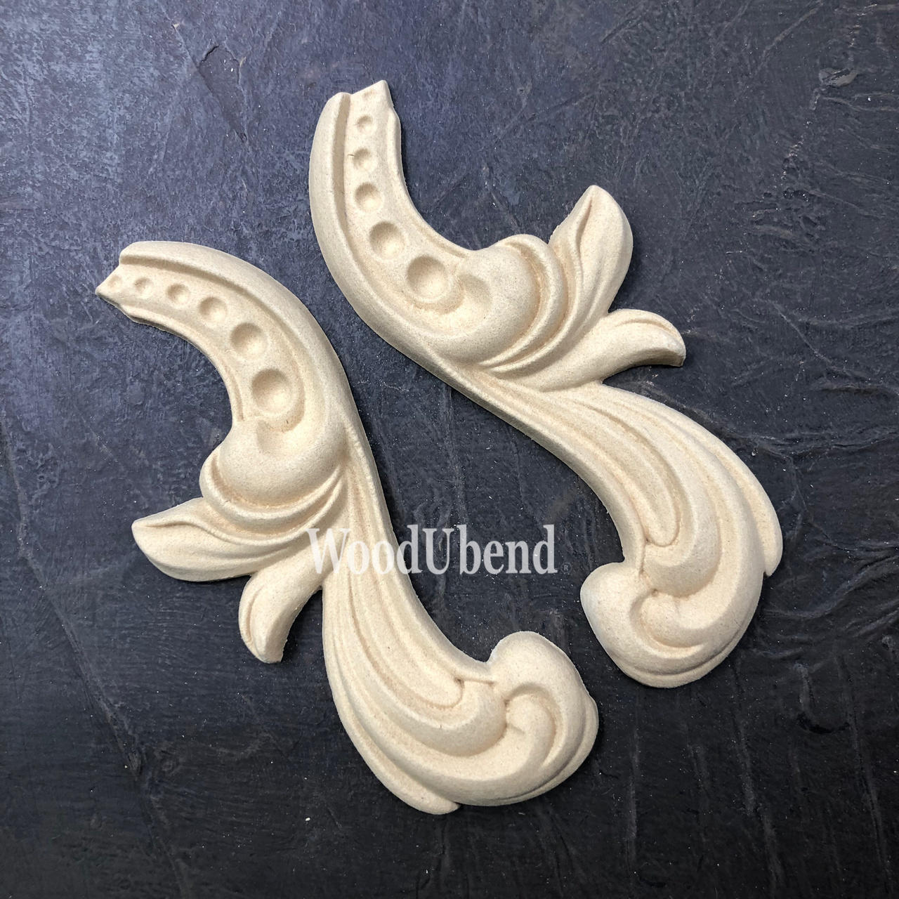 WoodUBend Applique #6096 (set of 2) is the perfect mouldable embellishment for any project!
The  Applique #6096 (set of 2) is seen side by side out of their packaging on a black crinkled background.