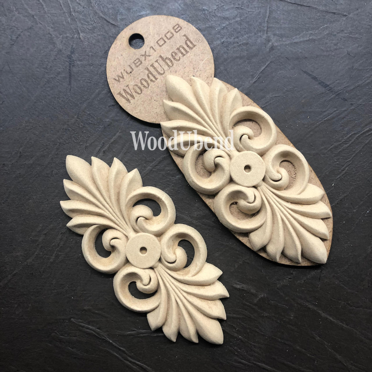 WoodUBend Applique #X1008 is the perfect mouldable embellishment for any project!
The Applique #X1008 is seen in its packaging and another side by side without packaging. Staged diagonally on top of a black crinkled background.