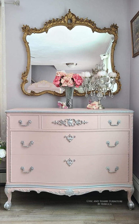 WoodUBend Fleur-de-lis Applique #2443 (set of 2) is the perfect mouldable embellishment for any project!
A pink dresser with the Fleur-de-lis Applique #2443 in silver going down the center of the drawers. Staged with a glass vase with pink flowers and a chandelier candle holders with flowers in the cups. A large gold framed mirror hanging above the dresser.