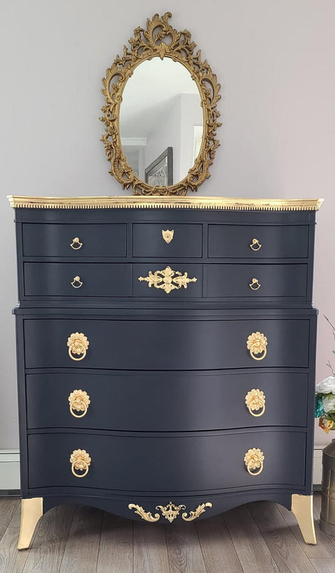 WoodUBend Fleur-de-lis Applique #2443 (set of 2) is the perfect mouldable embellishment for any project!
A black chest of drawers with the top, legs and as well as the hardware in gold. The Fleur-de-lis Applique #2443 on the bottom trim of the piece. Staged with a gold oval framed mirror.