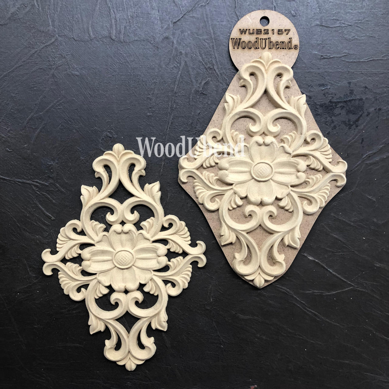 WoodUBend Floral Applique #2157 (set of 2) 
This is a set of two Appliques. These appliques are very intricate.  The center is solid with and oval middle, and two daisy pedals going out from the center at 3:00, 6:00, 9:00 and 12:00.  From the space between the "0" clocks there are flowing and curly "legs" .  When you look at the entire piece it reminds you of a fancy doorbell.  In this picture one of the appliques is out of the package and one is still in it's packaging.