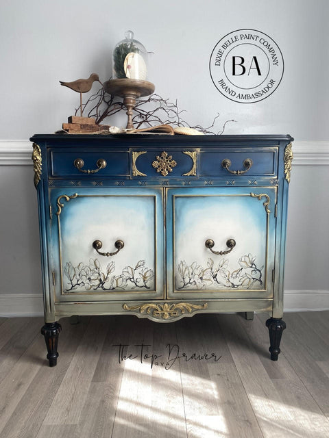 WoodUBend Floral Applique #2427 (set of 2) is the perfect mouldable embellishment for any project!
A credenza with the top of piece a dark blue going down to a mute green  with the middle front panels a blended white with Buds & Branches Transfer at the bottom. The  Floral Applique #2427 is seen on the top middle panel in-between two drawers painted gold.