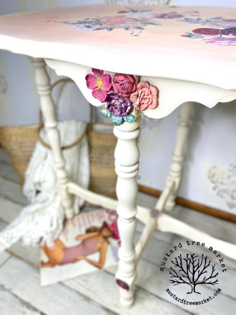WoodUBend Floral Applique #319 is the perfect mouldable embellishment for any project!
A white console table with Floral Applique #465 as well as Floral Applique #319 in a bunch on the front center of the table at the top of the leg. Staged with a magazine and a woven bag with a white blanket over the bag under the table.