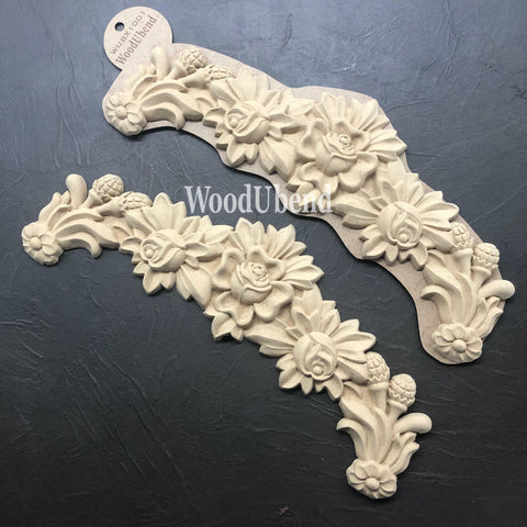 WoodUBend Floral Applique #X1001 is the perfect moldable embellishment for any project!
Two of The Floral Applique #X1001 side by side, one being in the packaging and the other is not. Staged on top of a black crinkled background.