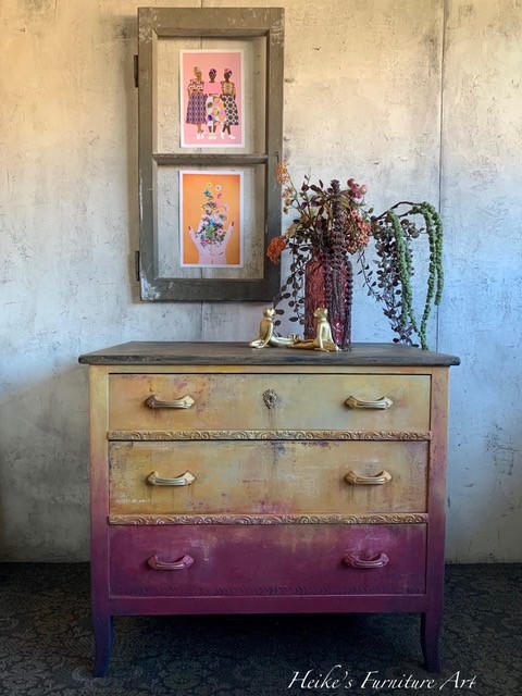 WoodUBend Keyhole #987 is the perfect mouldable embellishment for any project!
A dresser with the bottom drawer pink gradienting up towards a yellow/gold. The top drawer has Keyhole #987  in the center of the hardware and drawer. Staged with a red vase with flowers and two gold figurines on top of the piece.