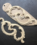 WoodUBend Ring Applique #1520 (set of 2) is the perfect mouldable embellishment for any project! A scroll style piece of wood applique placed beside each other angled to the left. The left applique is shown out of the package, and the right one is shown in the package.