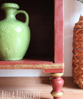 WoodUBend Trim #TR009 is the perfect mouldable embellishment for any project!  The lower right corner of a red shelf that has WoodUBend applied and highlighted gold.  A green vase sits on the shelf and a basket is to the right of the piece.