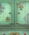 WoodUBend Trim #TR50a is the perfect mouldable embellishment for any project!  A section of a green chalk painted cabinet that has several different WoodUBend moulds applied to it and accented in gold gilding wax.  A Fleur-de-lis rub on transfer is applied to the doors, and a stencil pattern is chalk painted to the front of the piece in multiple chalk painted colors.  The knobs are red.