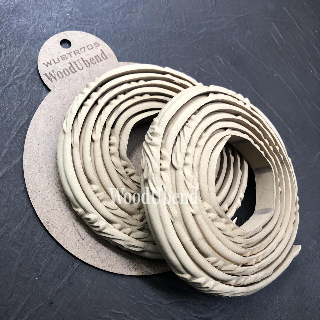 WoodUBend Trim #TR705 (Set of 2) is the perfect mouldable embellishment for any project!  Two rolled up strips of WoodUBend lying on top of a brown round piece of paper with WoodUbend WUBTR705 printed at the top.  All are placed on top of a black table.