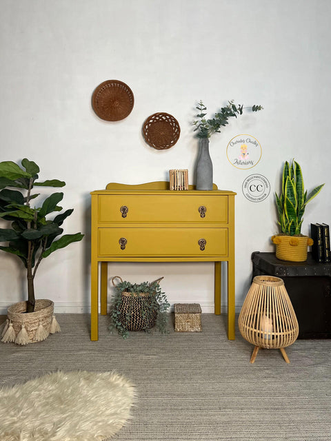 Yellow painted two drawer dresser transformation with bronze pulls. Staged with a gray textured vase containing faux greenery and a bamboo candle holder on top.