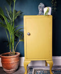 Yellow painted cabinet makeover with a silver knob. Staged with a white pot and a patinaed Buddha on top.