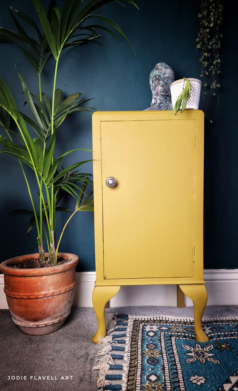 Yellow painted cabinet makeover with a silver knob. Staged with a white pot and a patinaed Buddha on top.