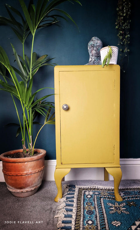 Yellow painted cabinet makeover with a silver knob. Staged with a white pot and a patinaed Buddha on top.