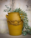 Large yellow painted pot containing faux greenery.