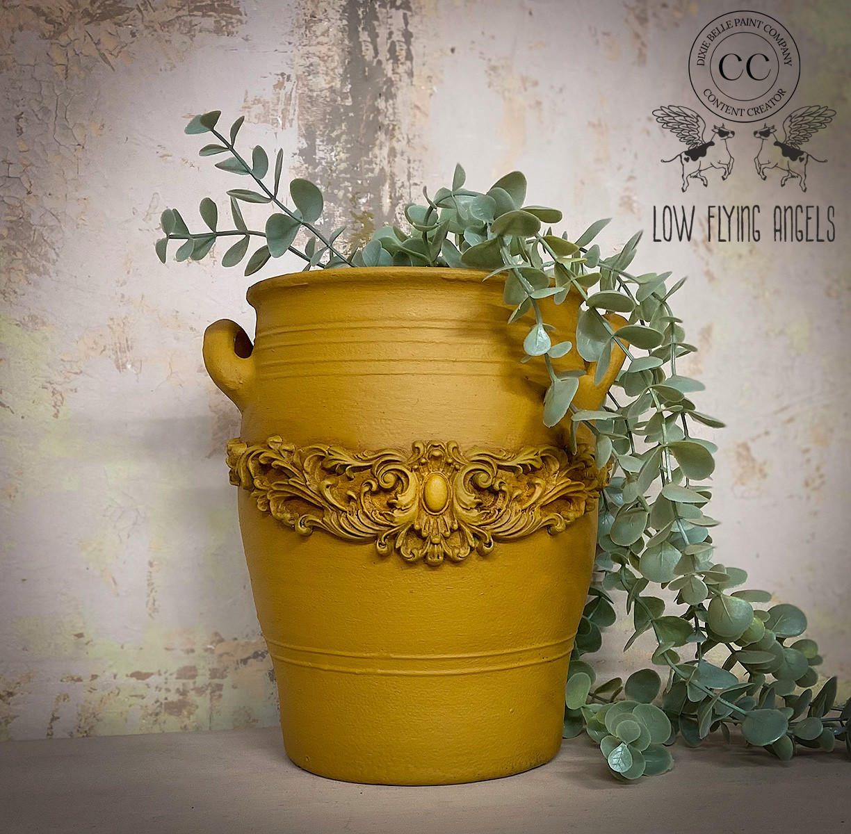 Large yellow painted pot containing faux greenery.